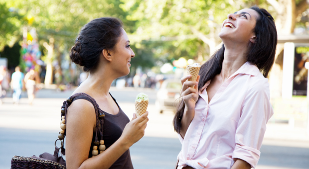 Foto på två tjejer som skrattar och äter glass i en stad.