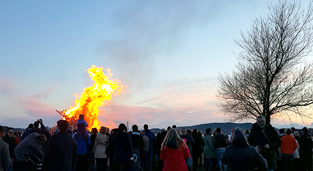 En folkmassa står och tittar på en brinnande påskbrasa