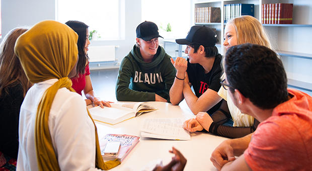 Foto av elever som samtalar vid ett bord i Gullmarsgymnasiets bibliotek