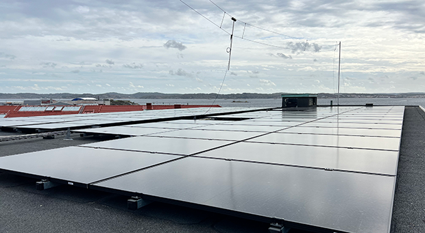Svarta solcellspaneler på ett platt tak med havet i bakgrunden